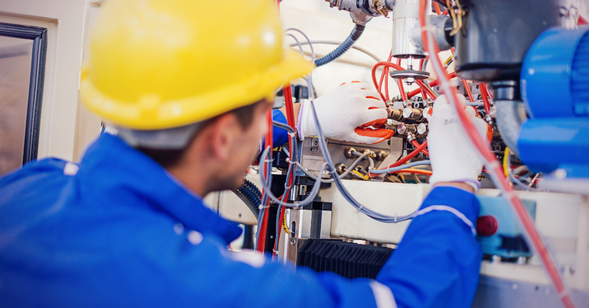 Engineer wearing a yellow hard hat and protective gloves working on electrical and mechanical integration with industrial machinery
